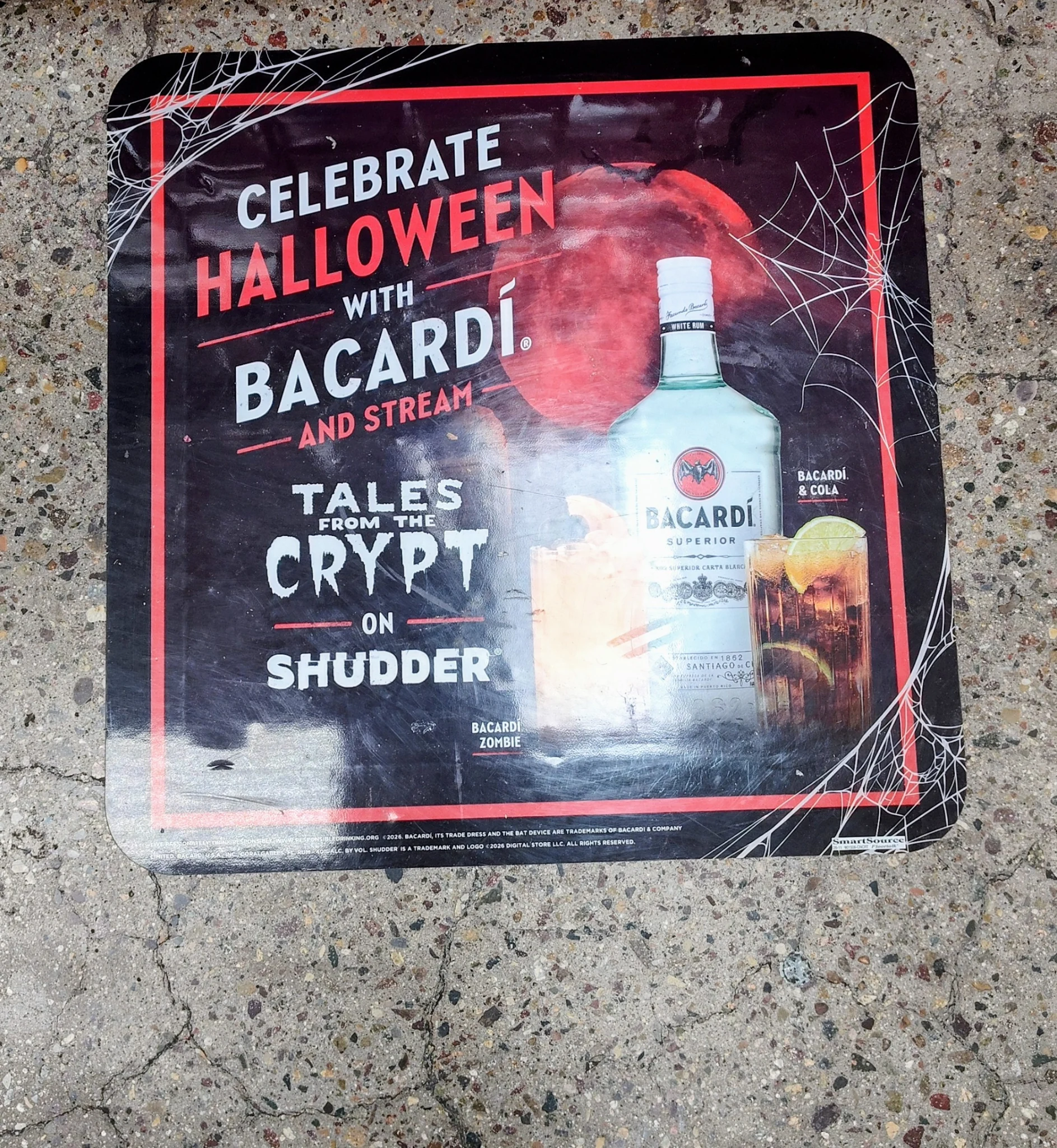 Close-up of Bacardí Halloween retail media floor advertisement at Ralphs promoting Tales from the Crypt on Shudder, with spiderweb graphics and Bacardí Superior bottle.