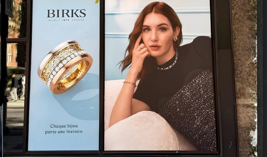 BIRKS fine jewelry street-level OOH advertising with gold rings, the French message Chaque bijou porte une histoire and a model wearing jewelry.