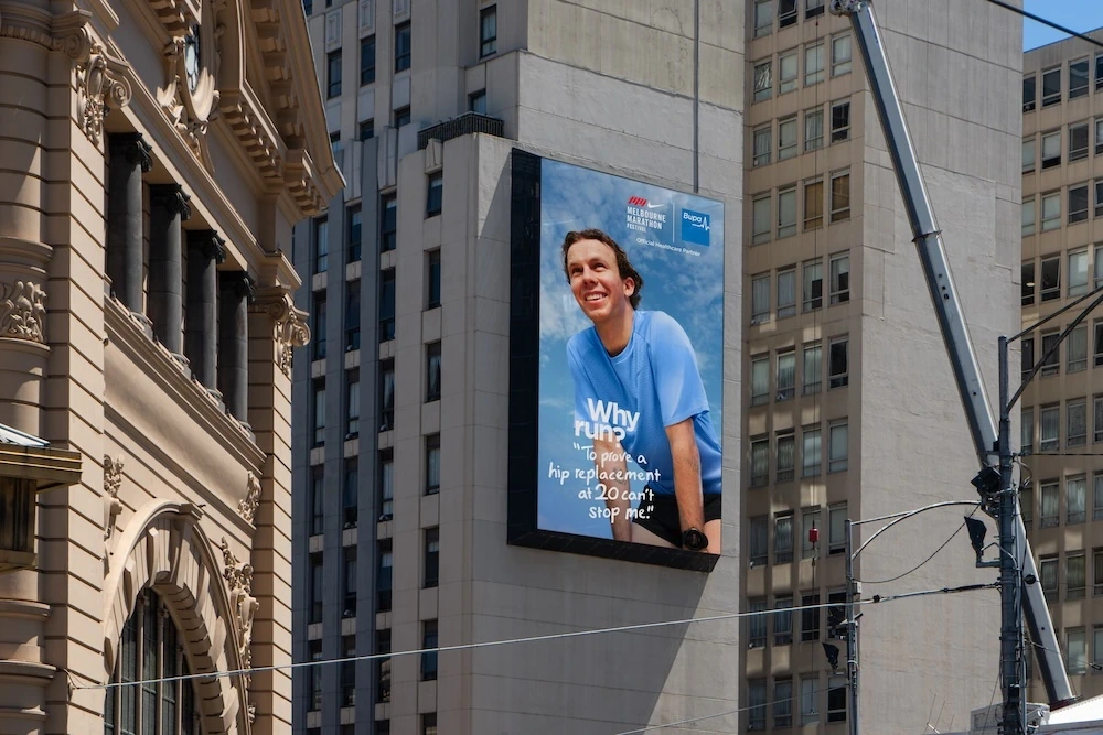 Vertical Bupa billboard in Melbourne featuring a runner and the message Why run? To prove a hip replacement at 20 can’t stop me.