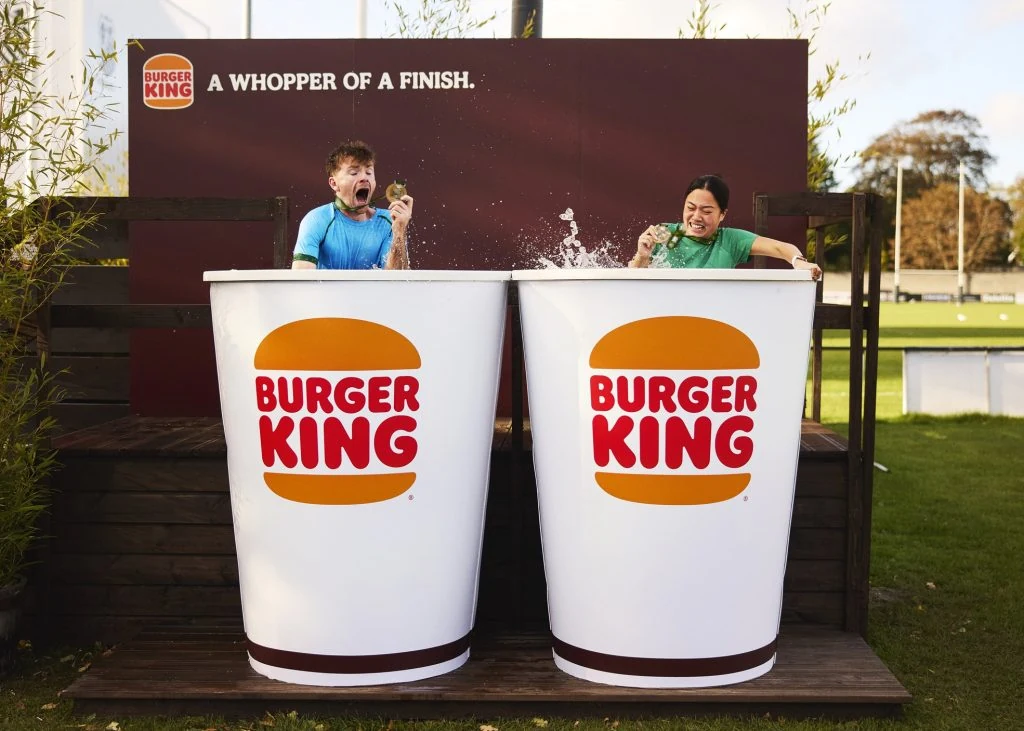 Two Dublin marathon participants in Burger King-branded cold plunge tubs under an A Whopper of a Finish outdoor activation sign.