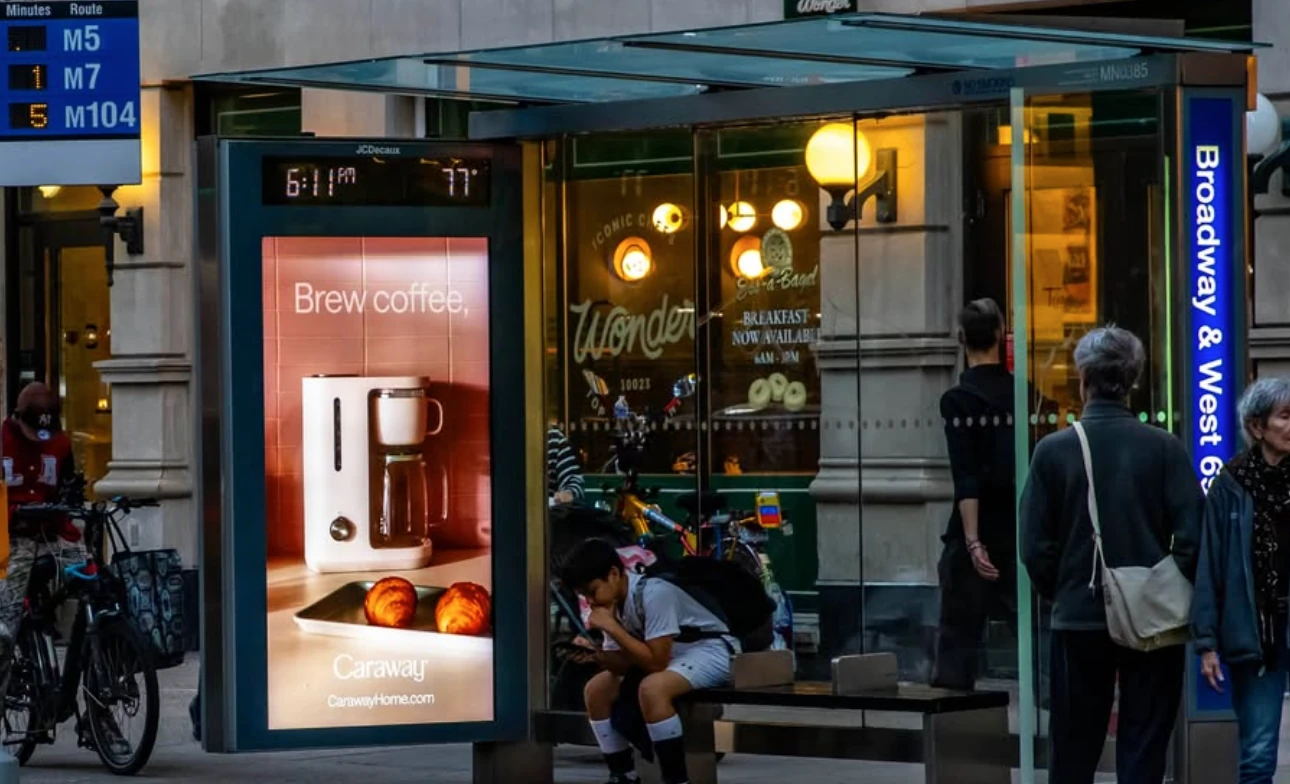 Caraway Home coffee maker advertisement displayed in a bus shelter with a warm kitchen image.