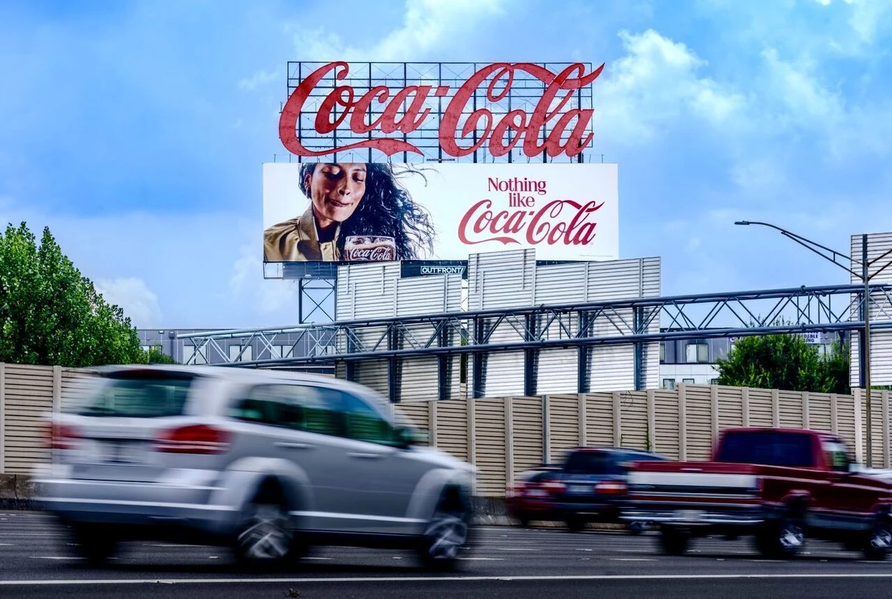 Coca-Cola roadside billboard reading Nothing like Coca-Cola beneath a large Coca-Cola script sign beside moving highway traffic.