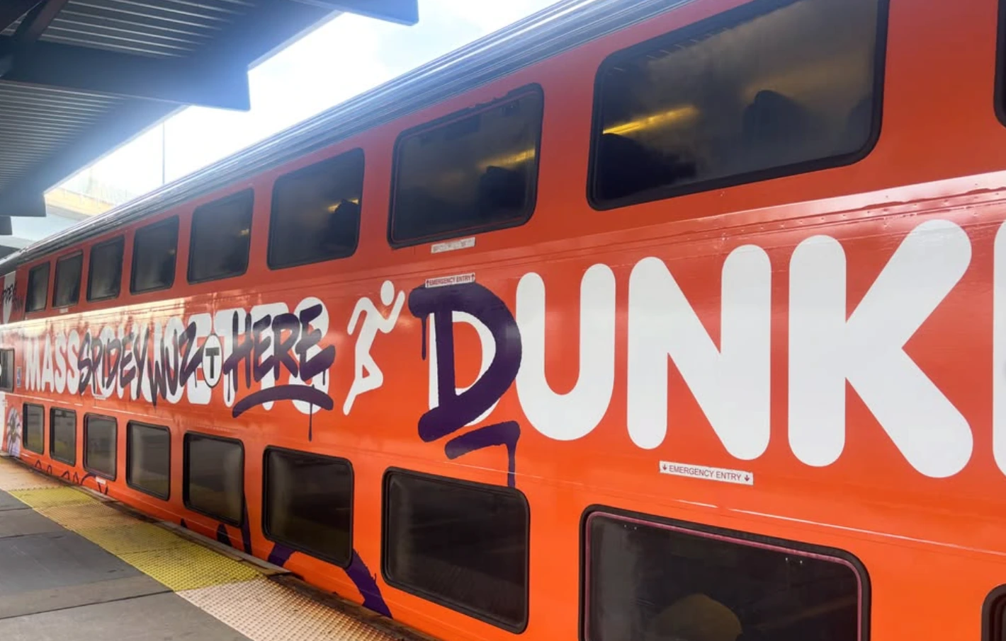 Bright orange Dunkin’ wrap covering an MBTA double-decker train with large branding and hand-drawn graphics.