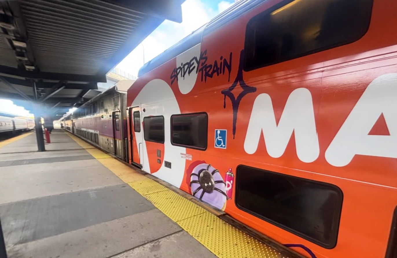 Dunkin’ orange MBTA train wrap seen from the platform with large seasonal artwork and full-vehicle branding.