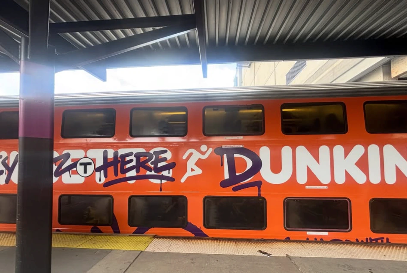 Dunkin’ MBTA train wrap showing orange seasonal branding, graffiti-style lettering and Spiders Train artwork.