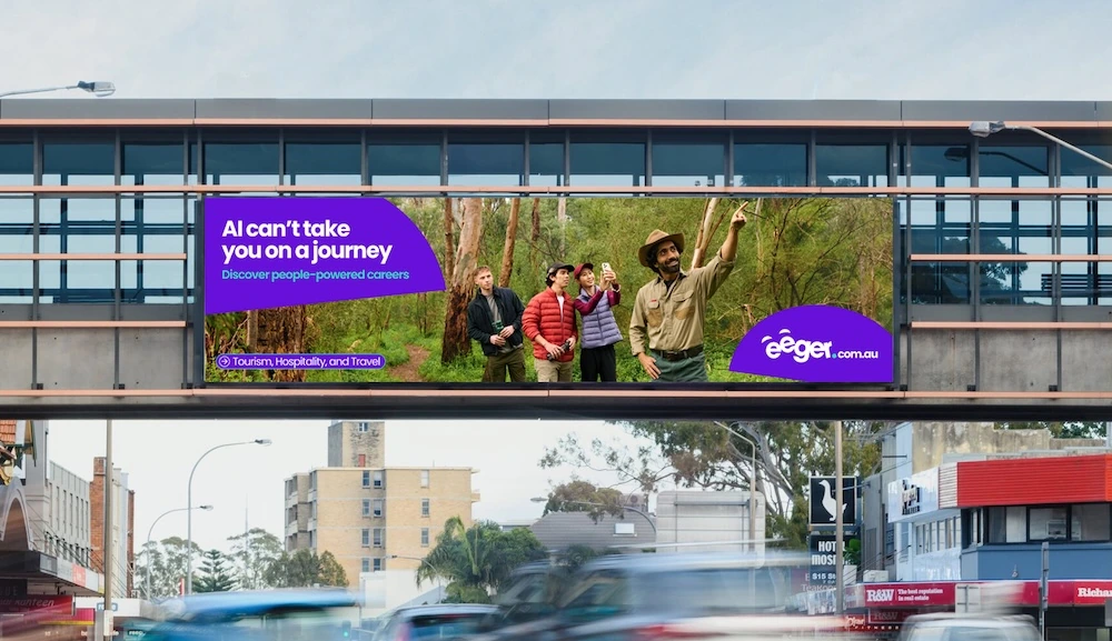 eeger outdoor billboard showing a tourism guide with visitors and the line AI can’t take you on a journey.