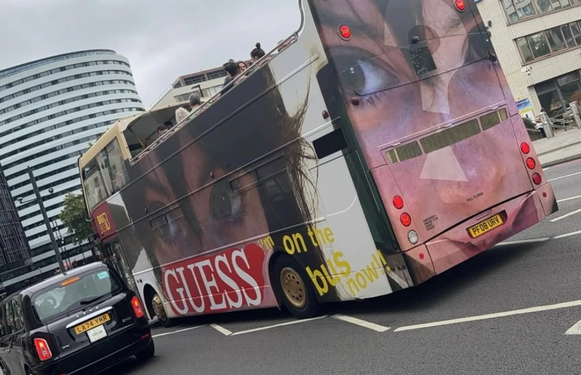 Guess Jeans double-decker bus in London featuring a close-up portrait and the phrase GUESS on the bus now.