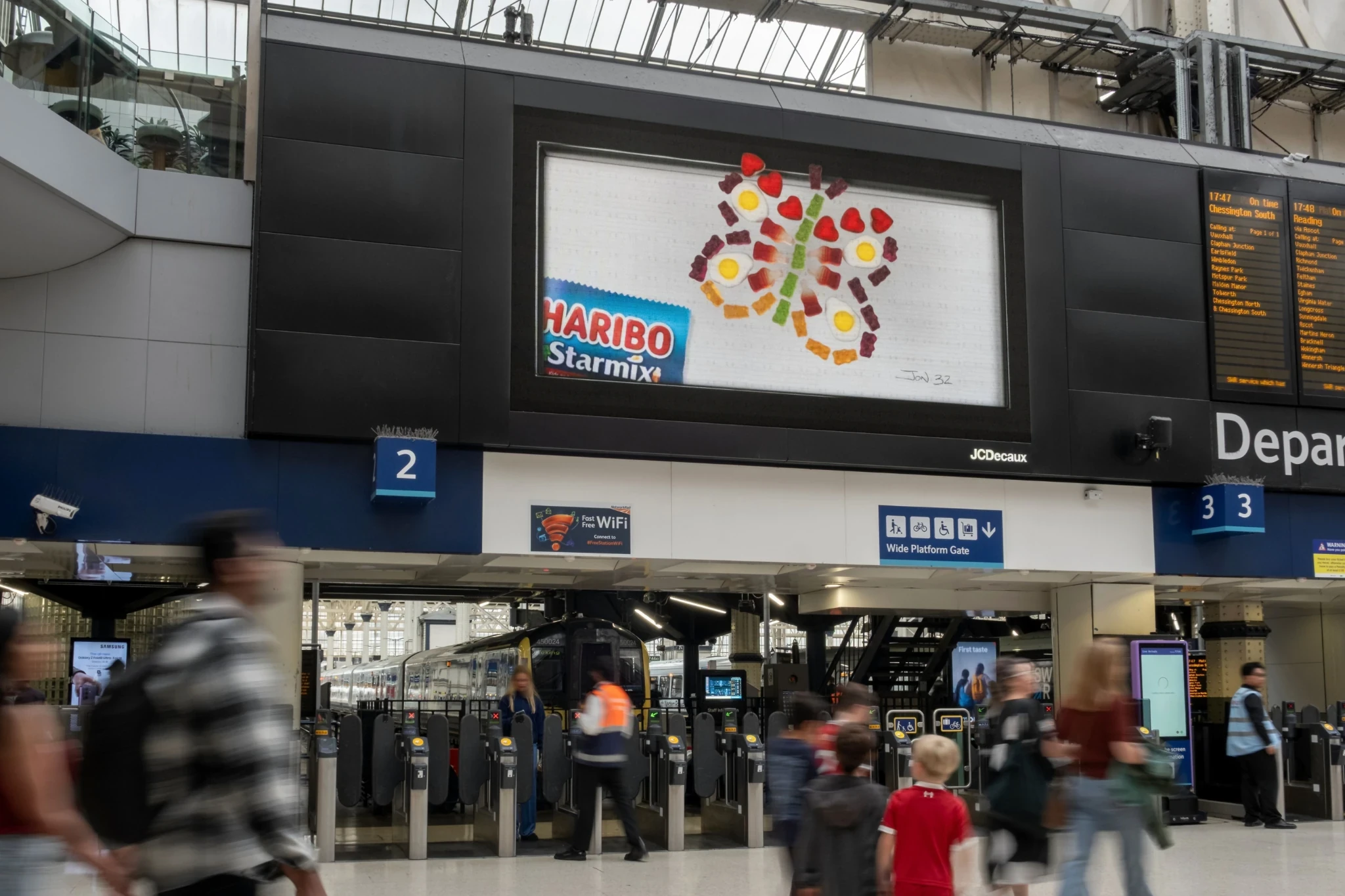 HARIBO Starmix OOH advertisement above a busy railway station entrance using colorful gummy shapes to create an imaginative figure.