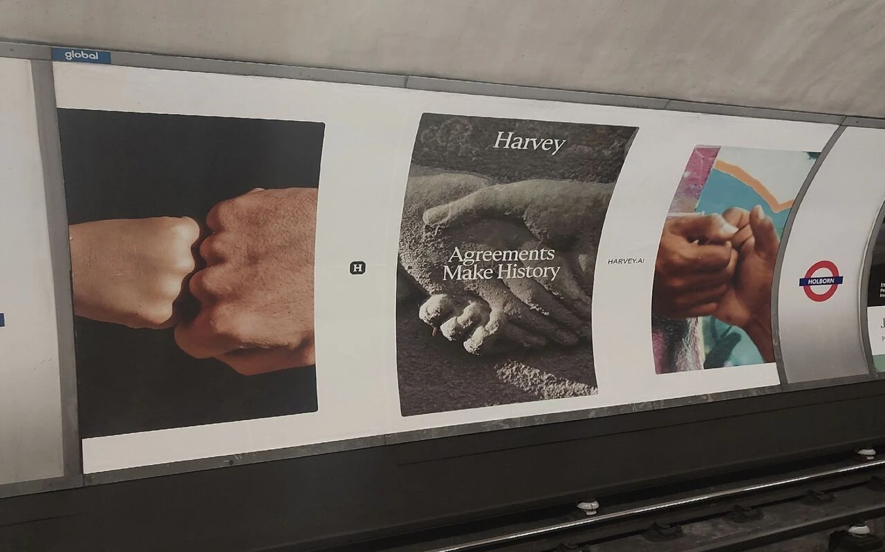 Harvey Agreements Make History OOH advertising posters installed at Holborn Underground station in London, showing close-up photographs of hands.