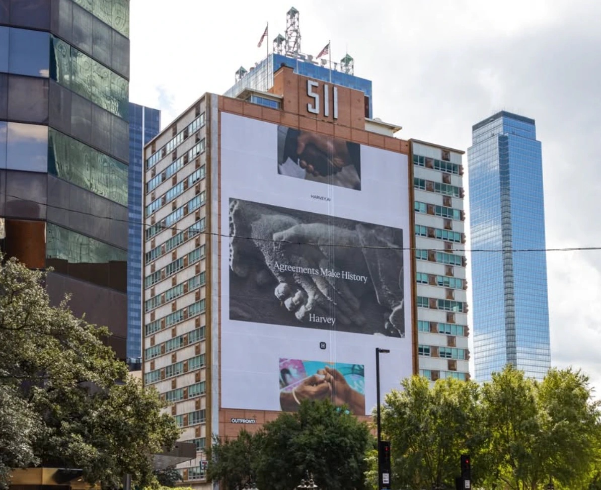Large Harvey Agreements Make History building wrap covering a tall city façade with multiple campaign images.