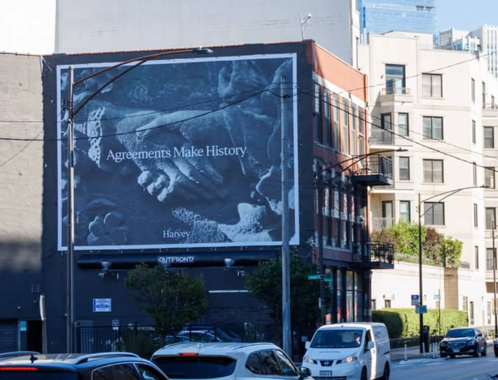 Harvey Agreements Make History roadside billboard displayed in a dense urban neighborhood.