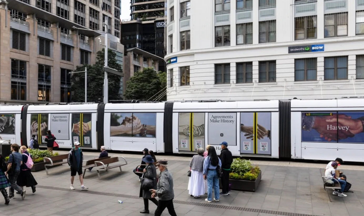 Harvey Agreements Make History campaign wrapped across a long urban transit vehicle with repeated hand imagery.