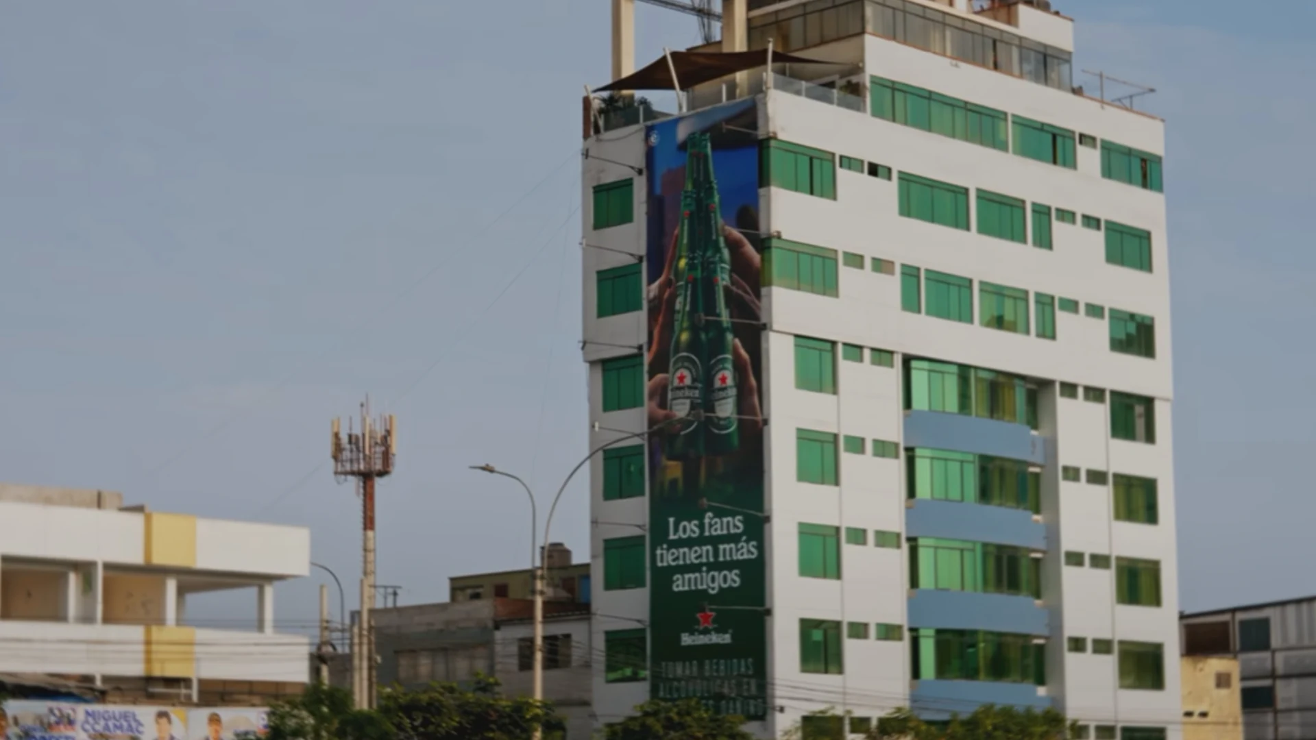 Heineken outdoor wallscape on a tall building in Lima, Peru, featuring green beer bottles and the message Los fans tienen más amigos.