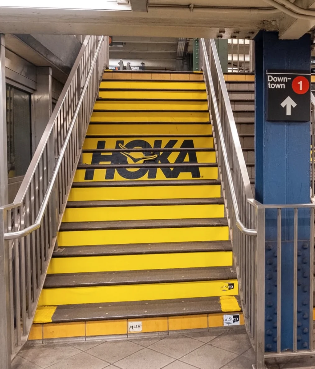 HOKA yellow staircase branding inside 59th Street–Columbus Circle subway station in New York City.