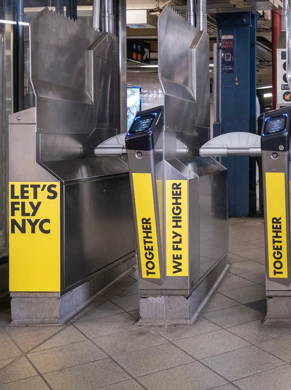 HOKA branded turnstiles at Columbus Circle with Together We Fly Higher and Let's Fly NYC messaging.