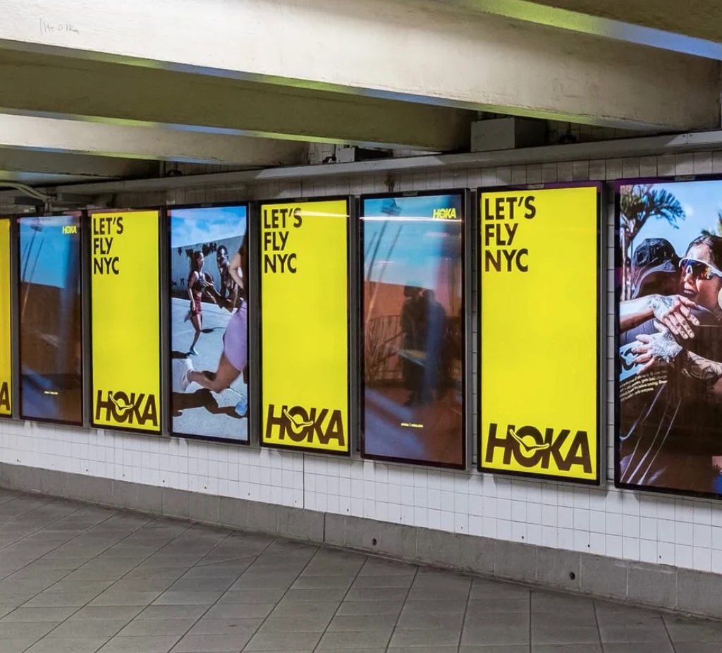 Row of HOKA subway advertising panels featuring Let's Fly NYC yellow creative and running photography.