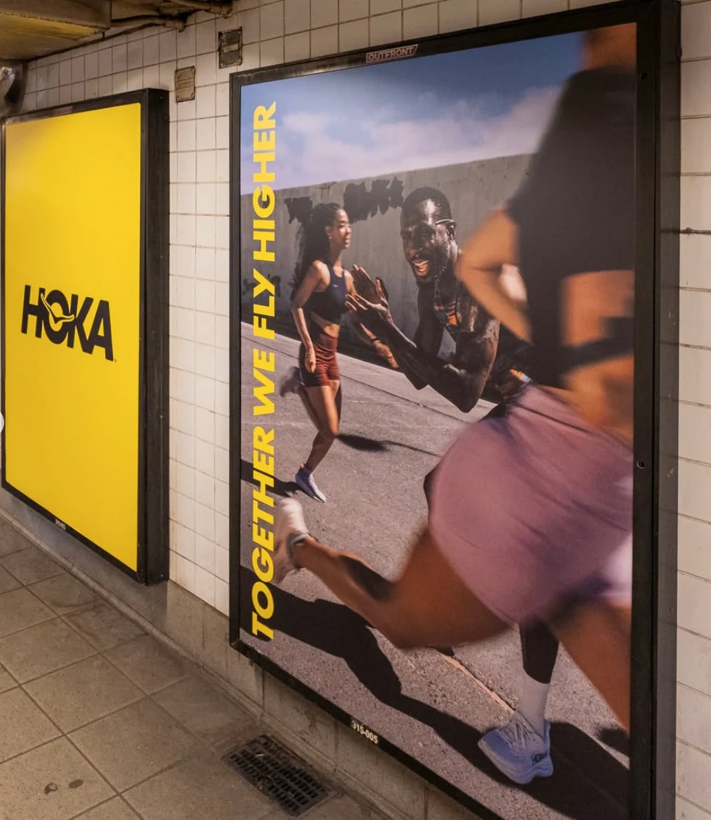 HOKA subway poster featuring runners and vertical Together We Fly Higher copy inside Columbus Circle station.