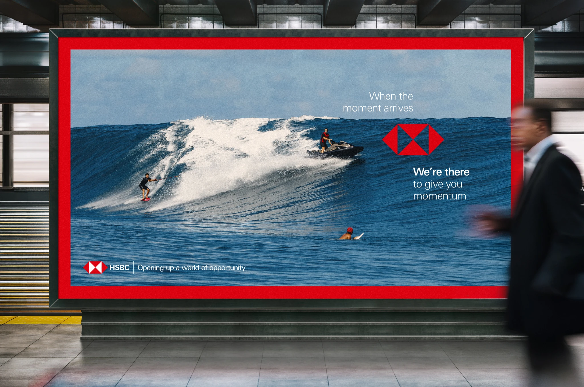 Large-format HSBC outdoor advertisement showing a surfer and jet ski driver on a large ocean wave with the message We’re there to give you momentum.