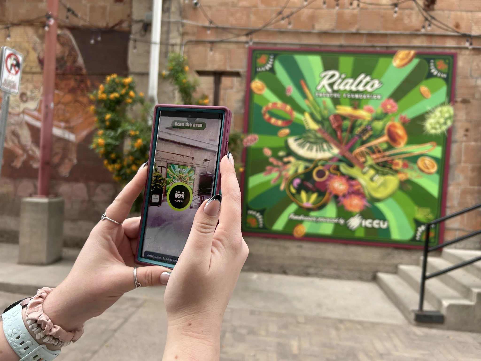 Visitor holding a phone to scan the ICCU Rialto mural in Tucson and start the browser-based augmented reality outdoor advertising fundraiser.