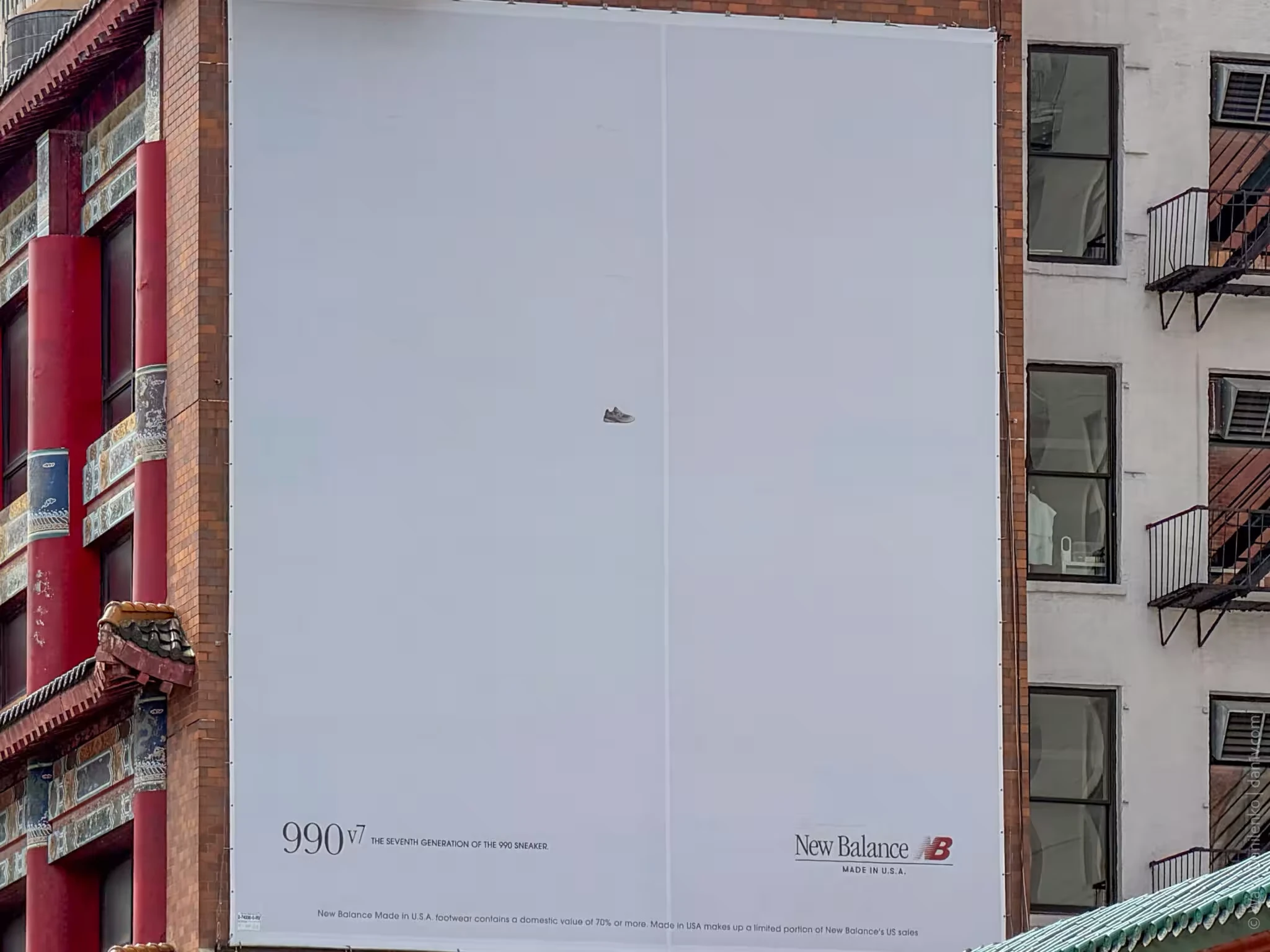 Large New Balance 990v7 billboard in New York dominated by blank pale space with a very small grey sneaker near the center.