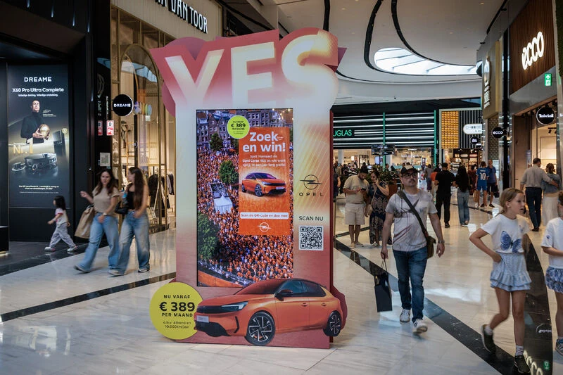 Opel Corsa special-build advertising installation inside a Dutch shopping mall featuring a large YES header, digital screen, QR code and coral-orange vehicle graphic.