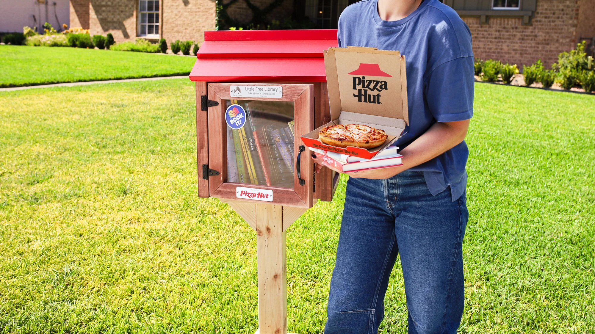 Pizza Hut Little Hut Library in a residential neighborhood with books inside and a person holding Pizza Hut pizza and books beside it.