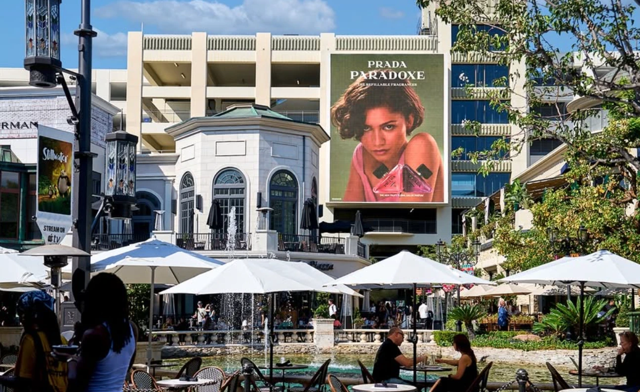 Prada Paradoxe large-format billboard overlooking a central plaza and dining area at The Grove in Los Angeles.