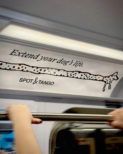 Spot and Tango Extend your dog's life campaign inside a New York City subway car with an elongated hand-drawn dog across the overhead advertising panel.