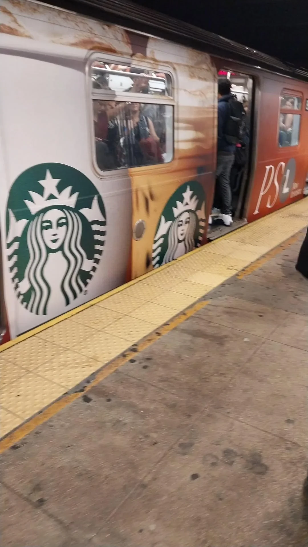 Starbucks Pumpkin Spice Latte wrapped MTA L train at a New York City subway platform with large Starbucks branding across the train exterior.