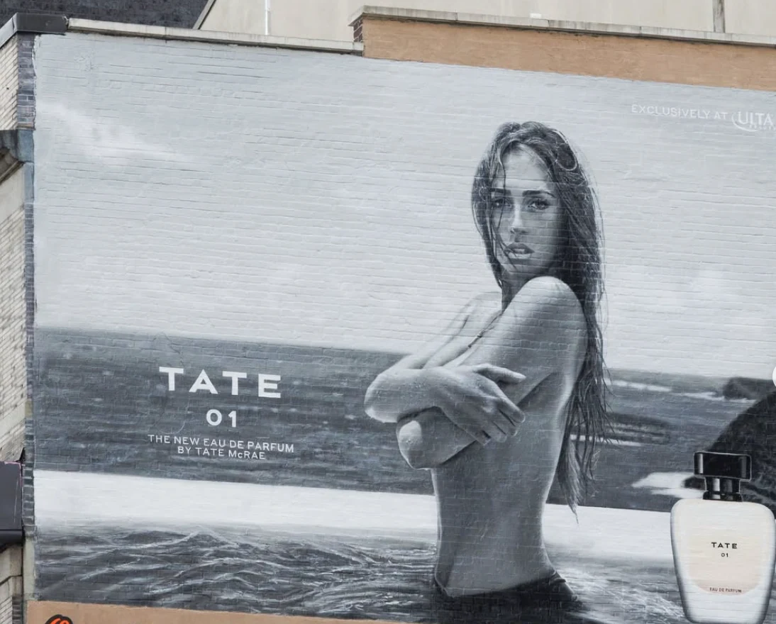 Close view of a Tate McRae TATE 01 fragrance wallscape in SoHo featuring monochrome portrait photography and the perfume bottle.