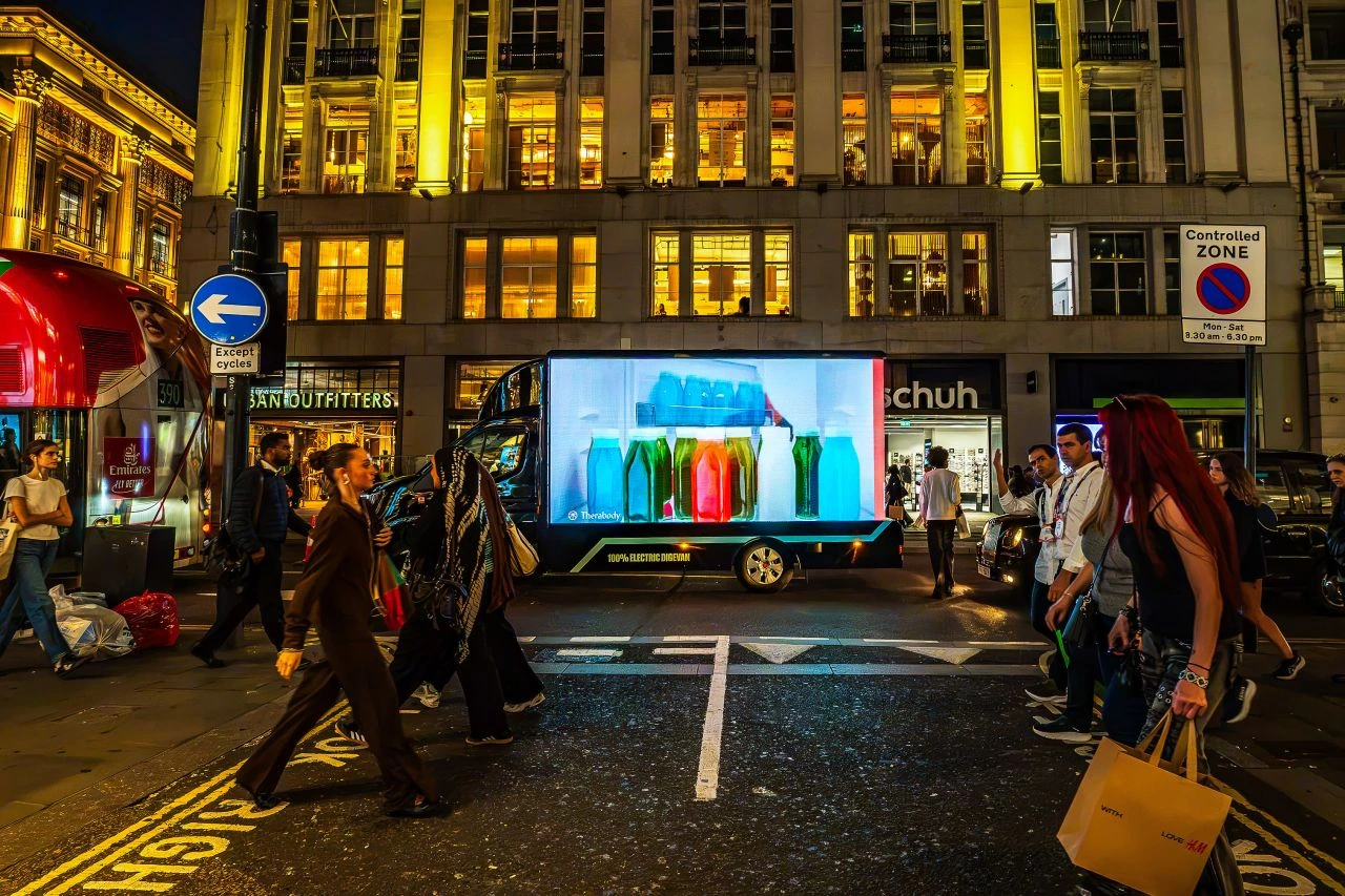 Electric Therabody digital advertising van displaying full-motion creative at night on a busy central London street.