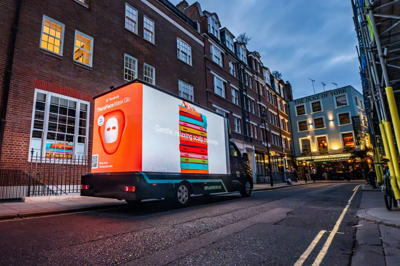 Therabody TheraFace Mask Glo campaign displayed on a three-sided electric digital advertising van driving through central London.