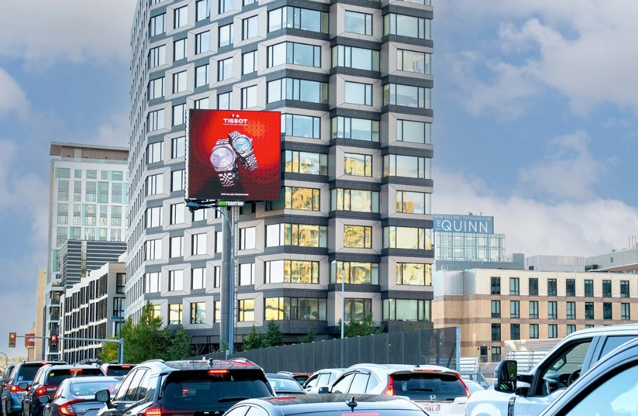 Tissot digital billboard above a busy Boston commuter route showing two watches against a red background.