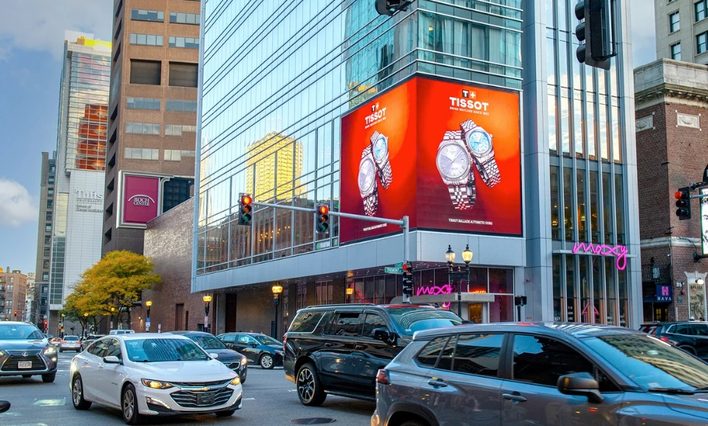 Tissot digital billboard in downtown Boston featuring two watches on a bold red background above a busy city intersection.