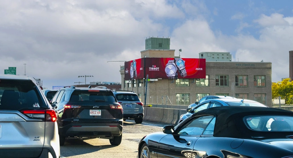 Wide Tissot digital billboard visible from a Boston highway with red creative and oversized watch photography.