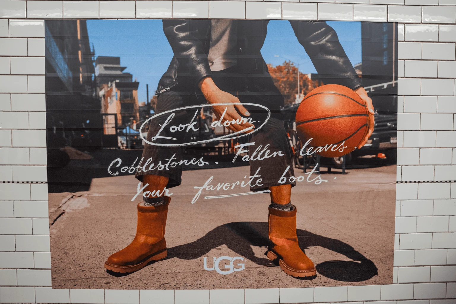 UGG Season subway advertising in New York featuring fall-themed copy, UGG boots and neighborhood-inspired creative inside a tiled transit environment.