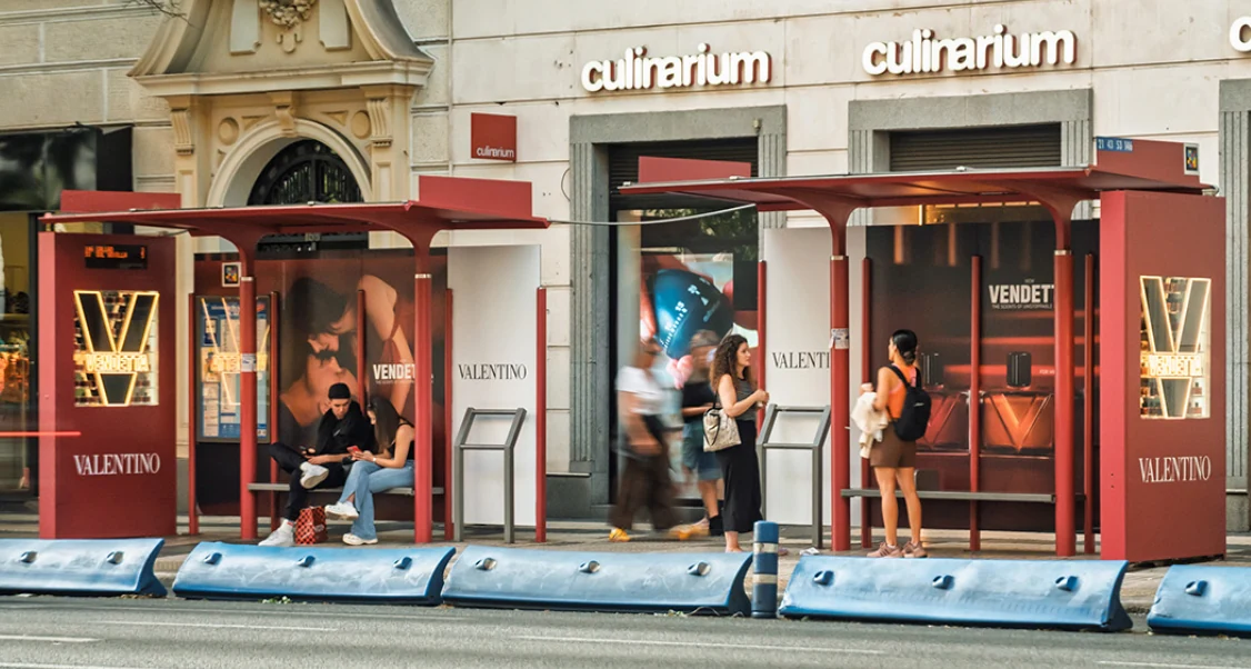 Two Valentino Vendetta red bus shelters with illuminated display cases and fragrance campaign creative in an urban street setting.