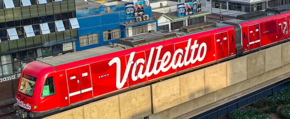 Side view of a red Vallealto wrapped Lima Metro train traveling on an elevated railway in Peru, displaying large white Vallealto branding.