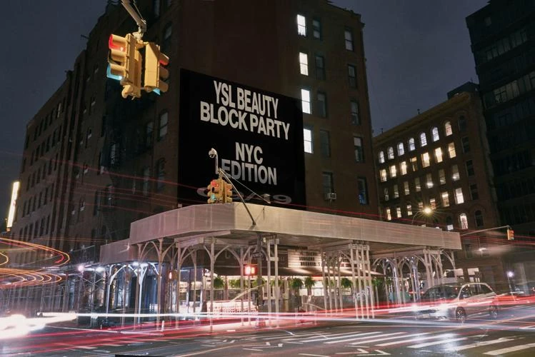 Large black YSL Beauty Block Party NYC Edition OOH advertisement displayed above a downtown New York street at night.